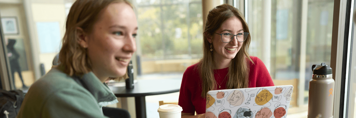 Two students sitting together with a laptop and coffees